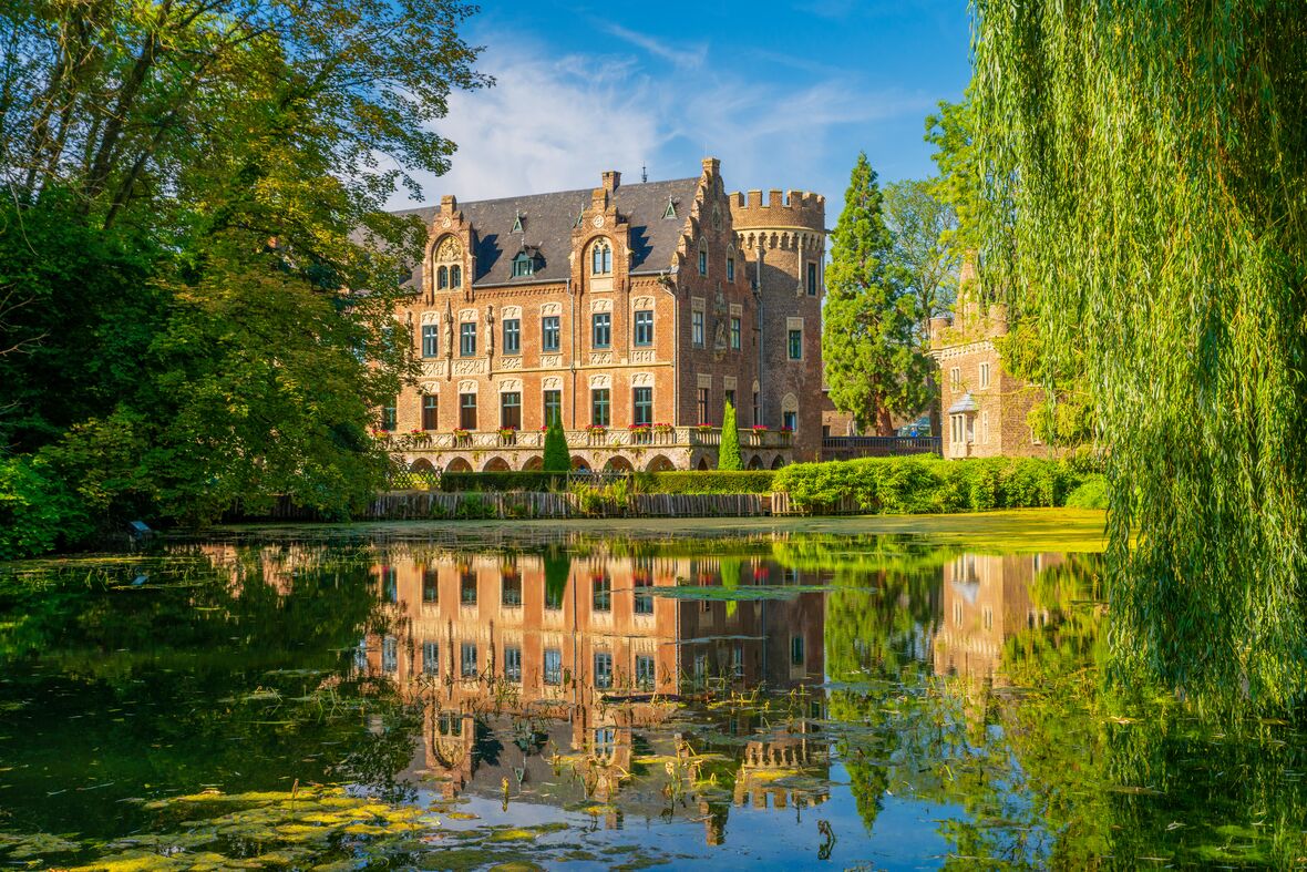 Schloss Paffendorf mit Parkanlage und Spiegelung im Wasser.